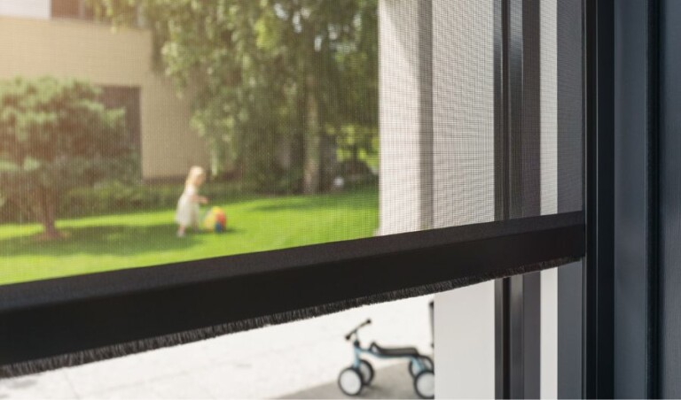 Detailaufnahme des schwarzen Abschlussstabs eines elektrischen Insektenschutzrollos mit feinmaschigem Gewebe und integrierter Bürstendichtung. Der Abschlussstab sorgt für einen sauberen unteren Abschluss und hilft, das Eindringen von Insekten zu verhindern. Die seitlichen Führungsschienen ermöglichen eine präzise und komfortable Bedienung des Rollos.