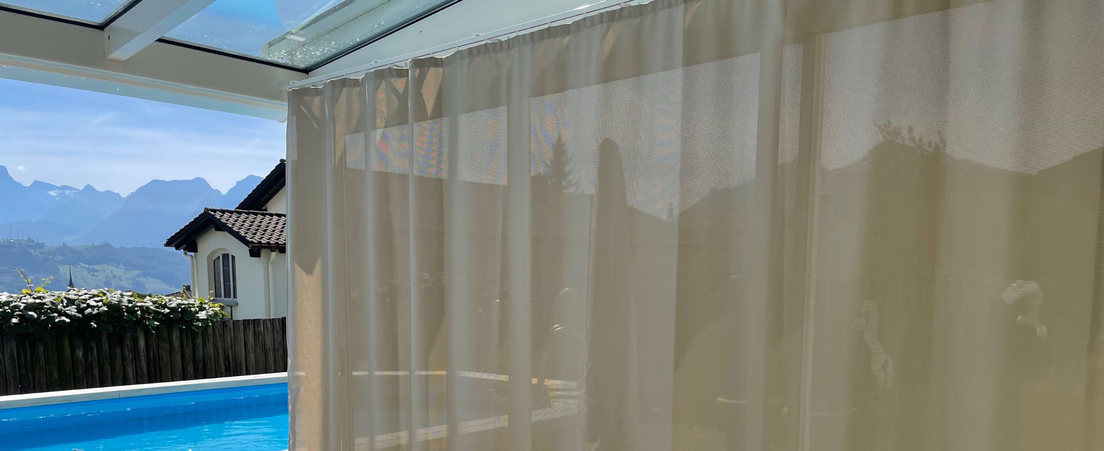 Terrasse mit transparentem Balkonvorhang entlang der Glasfront als Sonnen- und Sichtschutz.
